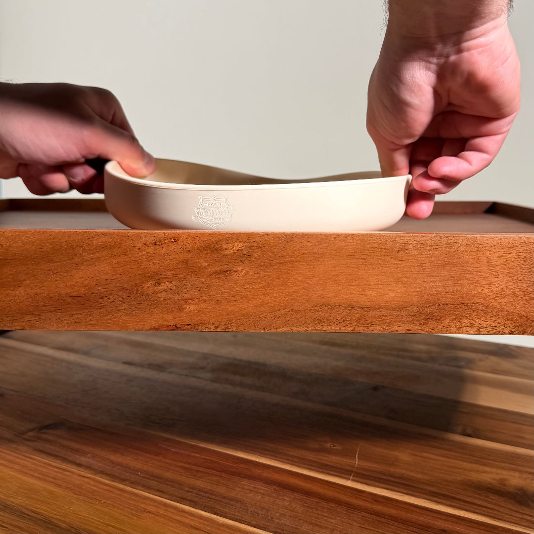 Beige silicone slow feeder bowl held by hands on a wooden surface