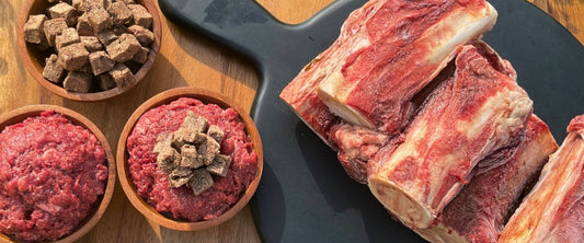 Midwest Legacy Beef meaty bones, raw dog food, and freeze-dried raw dog food and treats displayed on wood cutting board.