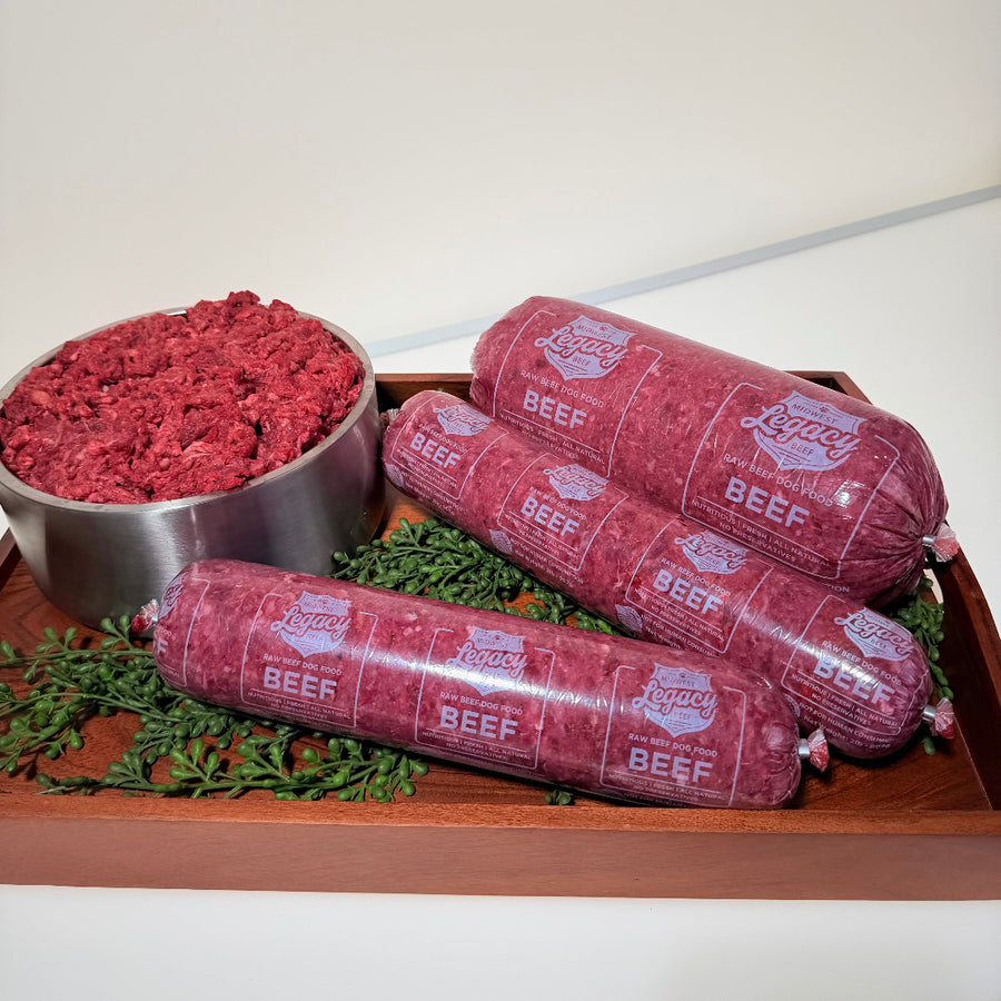 Raw beef logs on a wooden tray with ground beef in a metal bowl and herbs