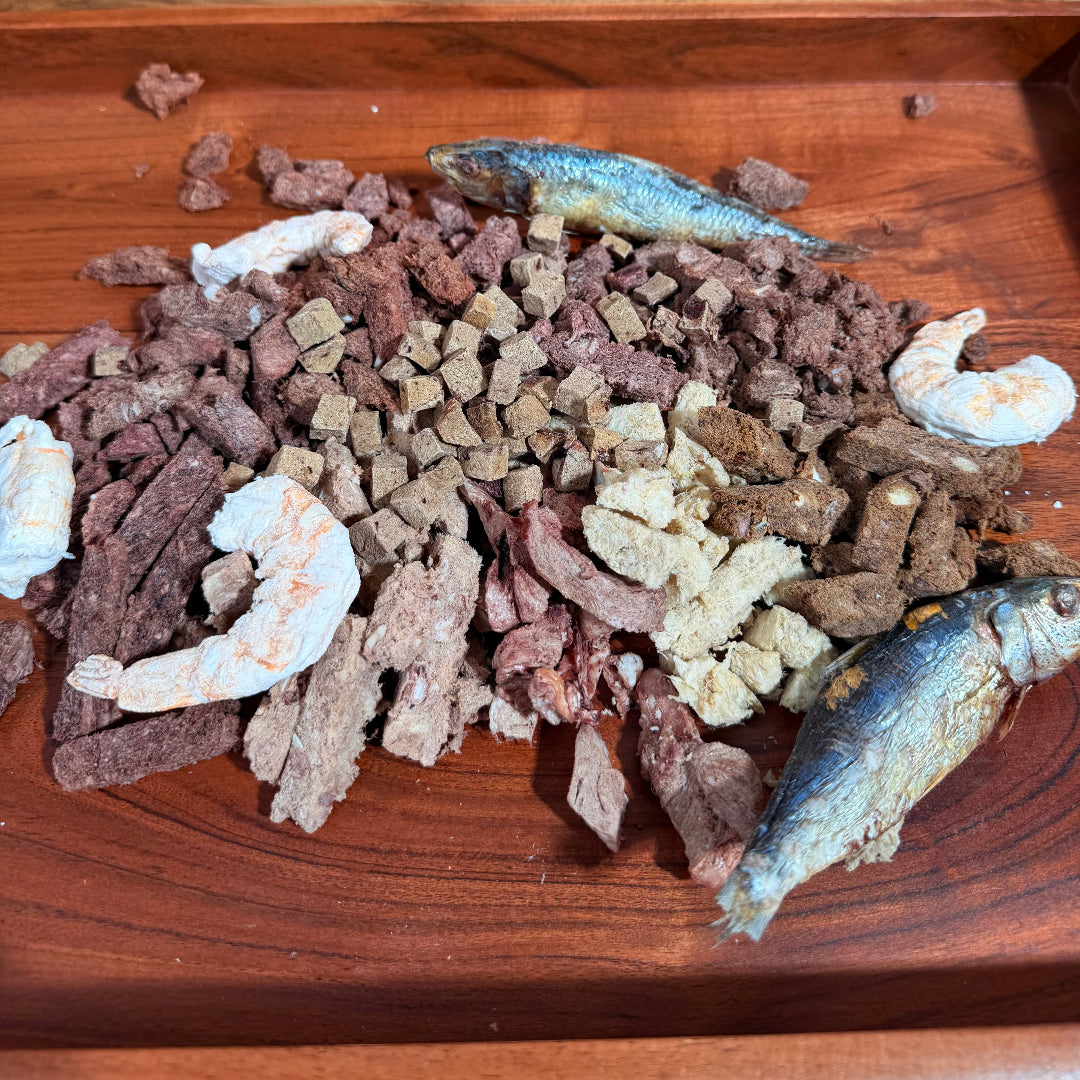 Loose freeze-dried pet food pieces and dried fish on a wooden tray.
