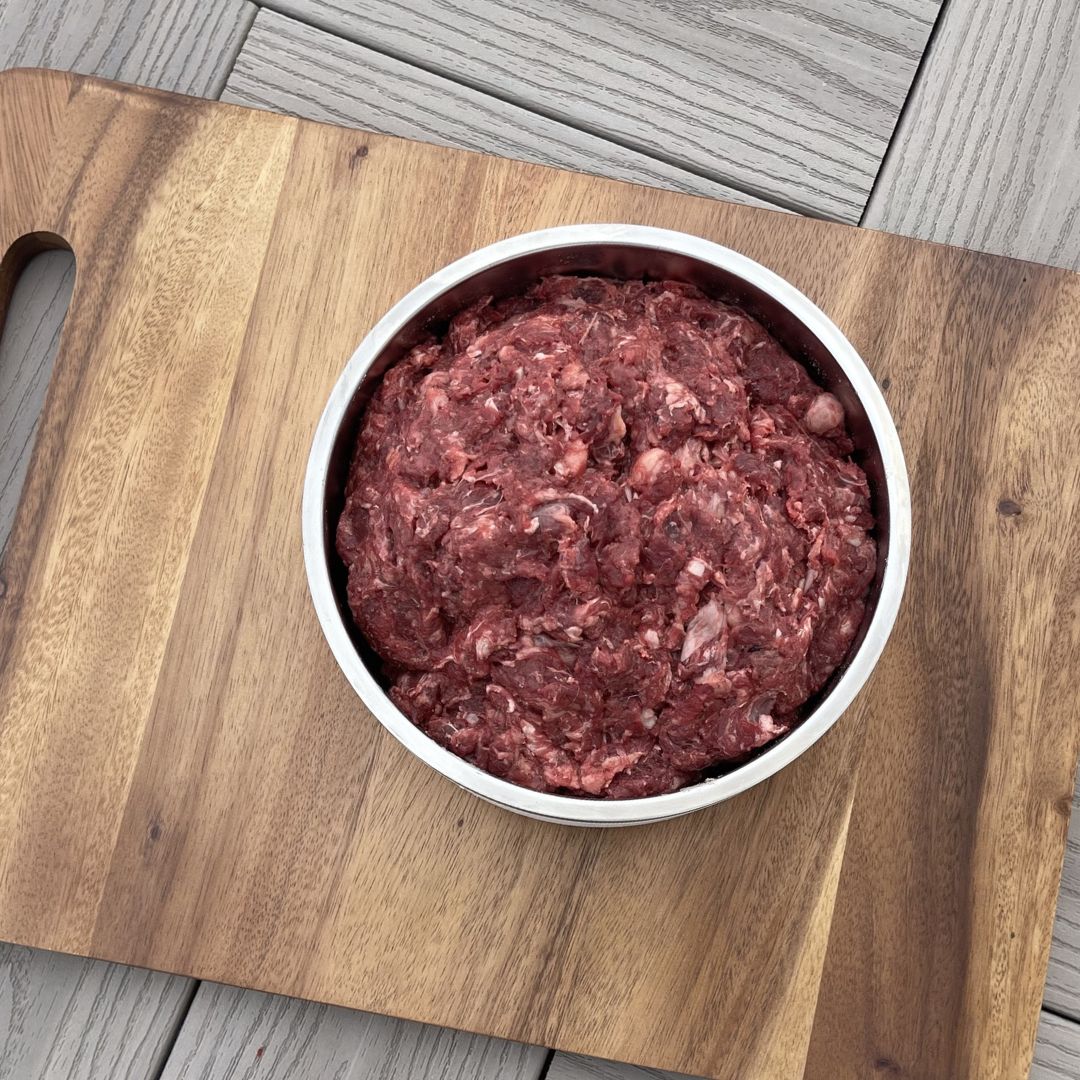 read and white chunky raw beef dog food in big bowl on wooden cutting board